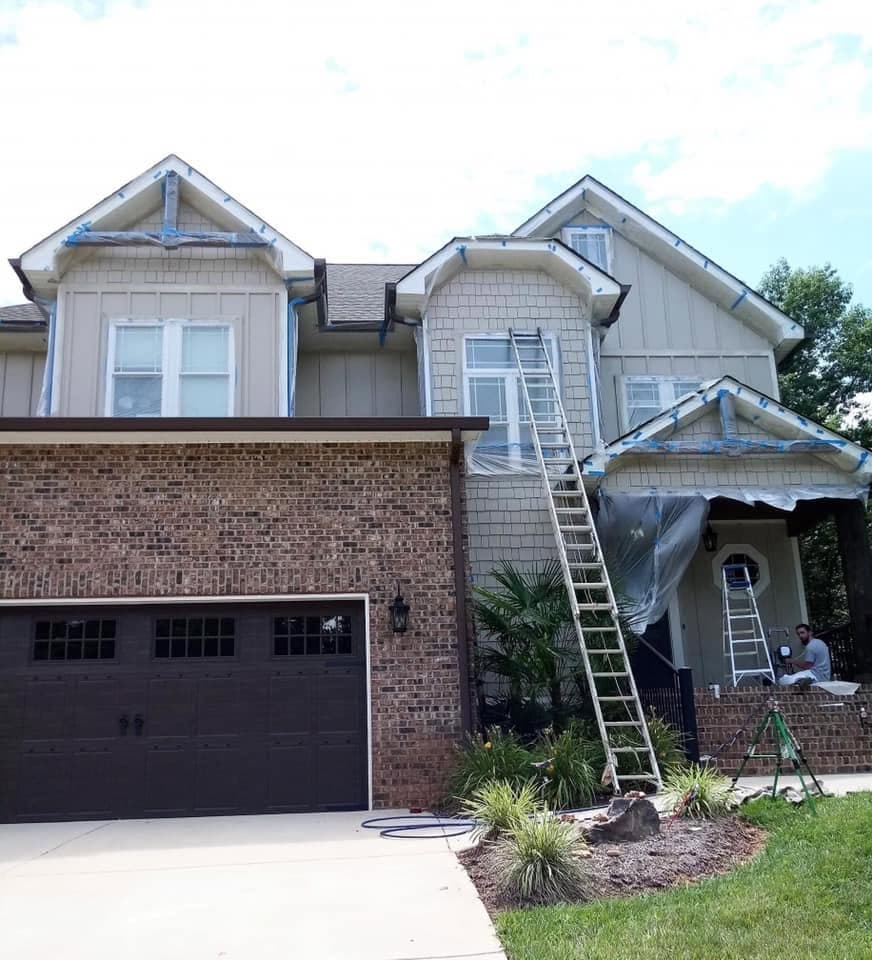 Two-story home with gables masked off and a ladder in place during an exterior repaint